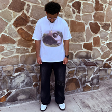 Load image into Gallery viewer, Person wearing a white t-shirt with a graphic design standing against a stone wall.
